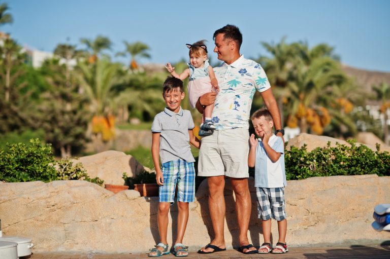 Man with three children posing outdoors in summer clothing.