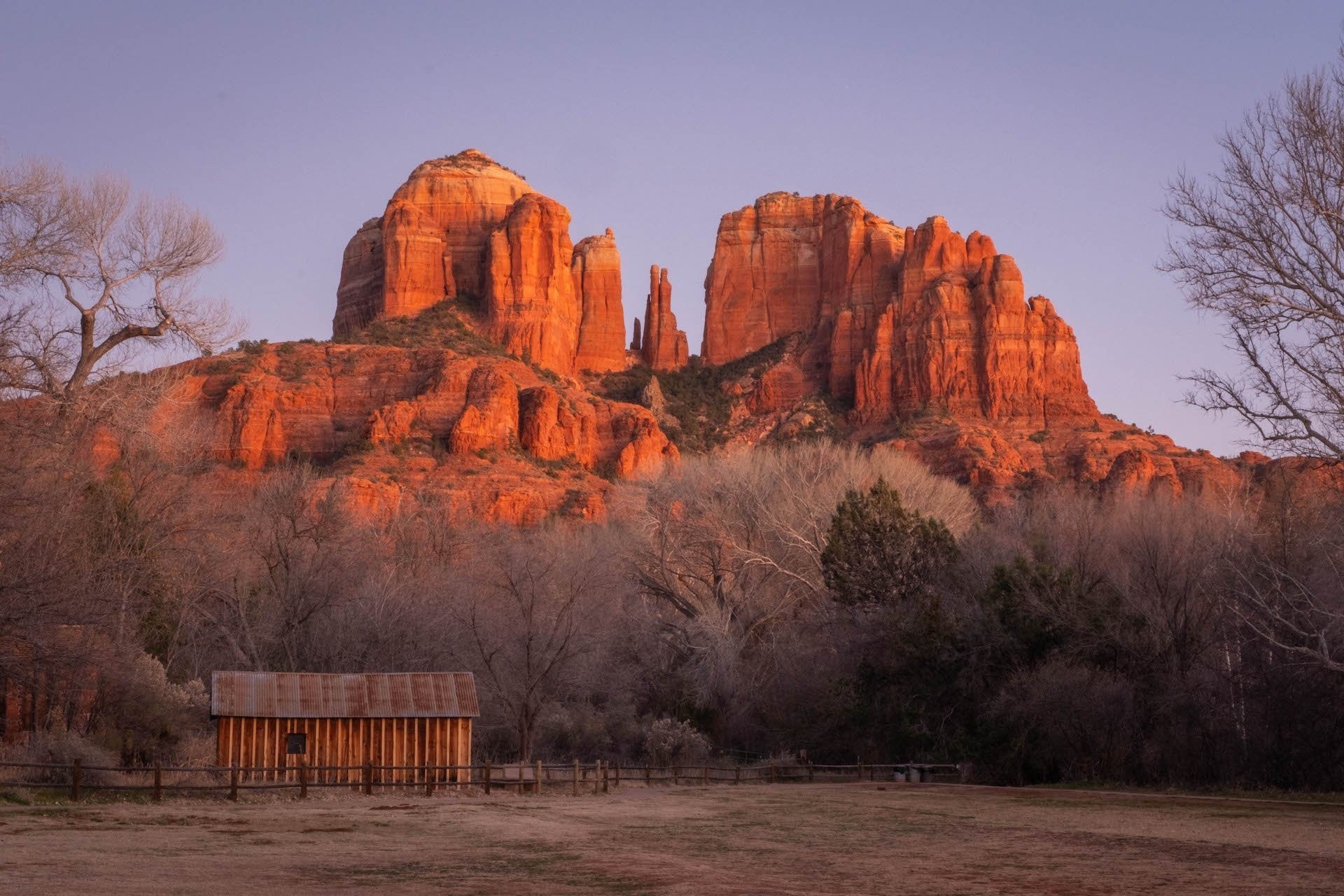 Wooden cabin in front of red rock formations at sunset.
