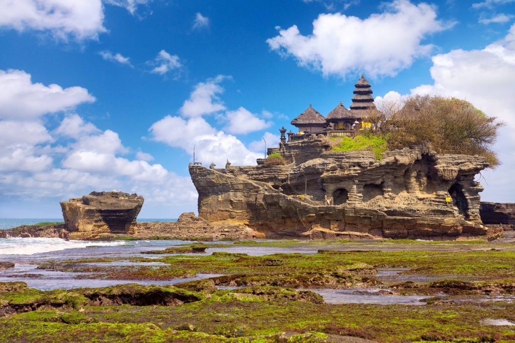 Temple on rocky shore with ocean and blue sky.