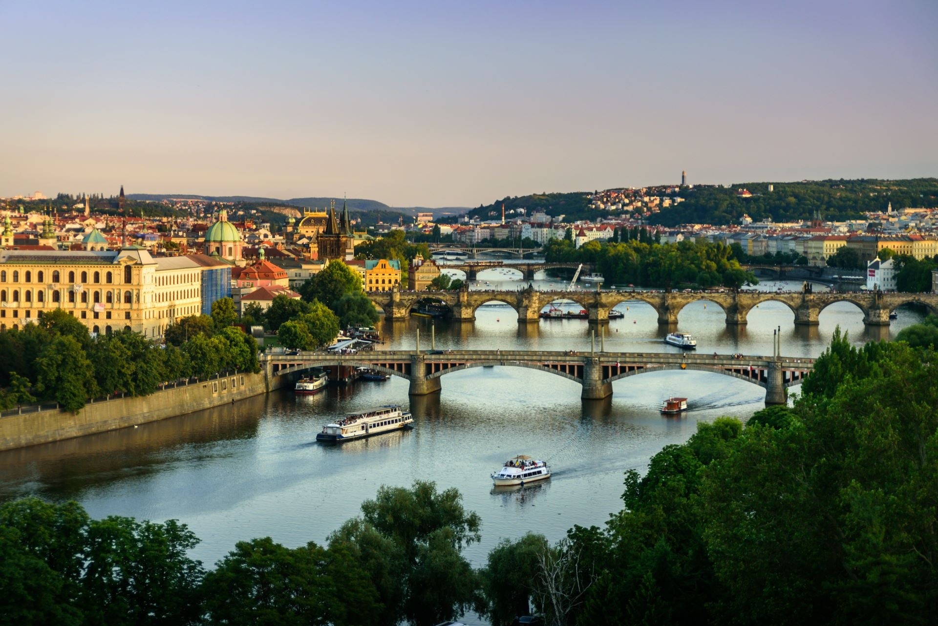 View of multiple bridges over a river with boats and cityscape in the background during sunset.