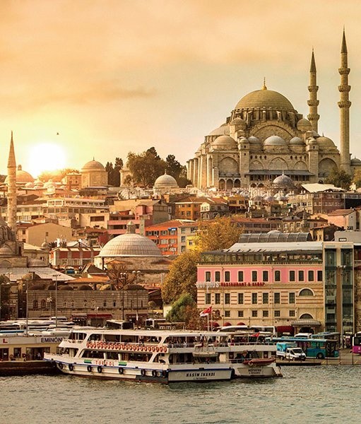 Sunset view of Istanbul skyline with boats on water and a large mosque with domes and minarets.