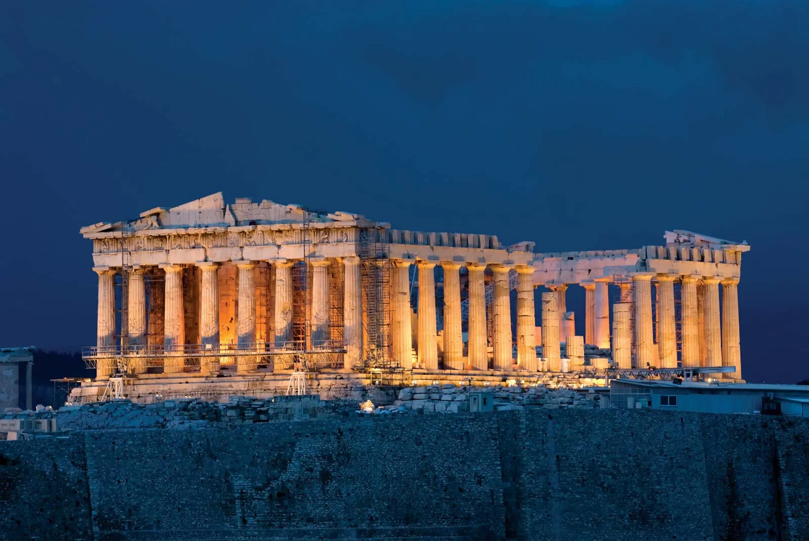 The Parthenon illuminated at night in Athens with a dark blue sky.