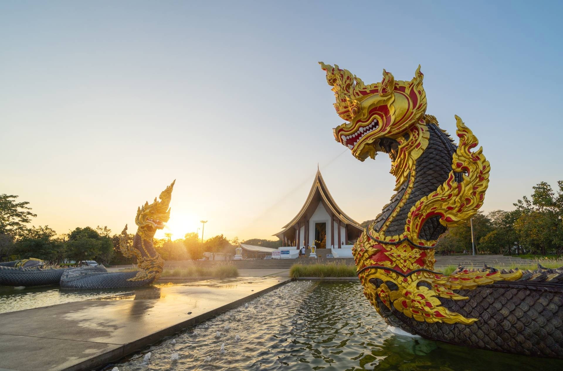 Ornate dragon statues in water near temple at sunset.