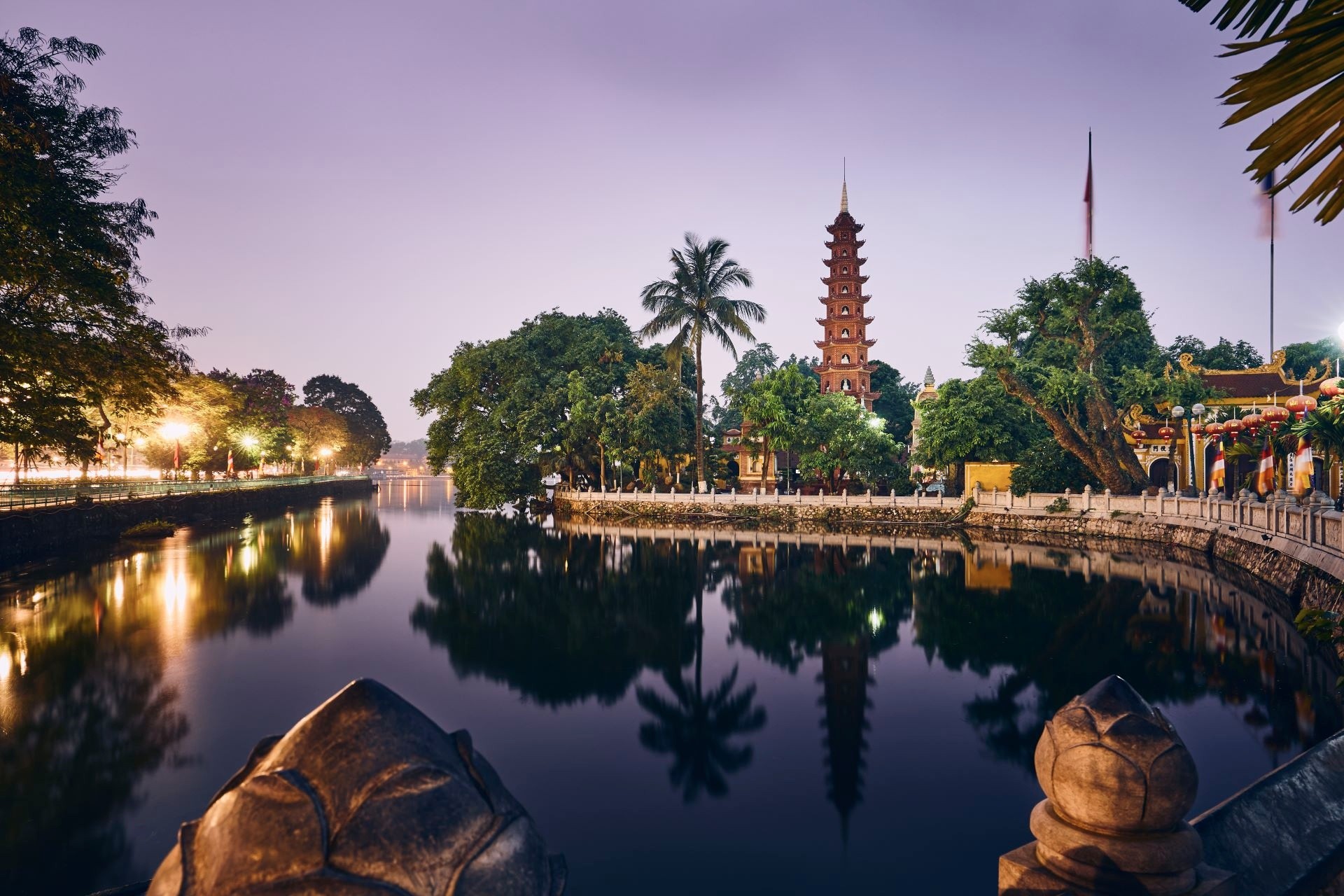 Tran Quoc Pagoda by a calm lake at dusk, with trees and soft lighting.
